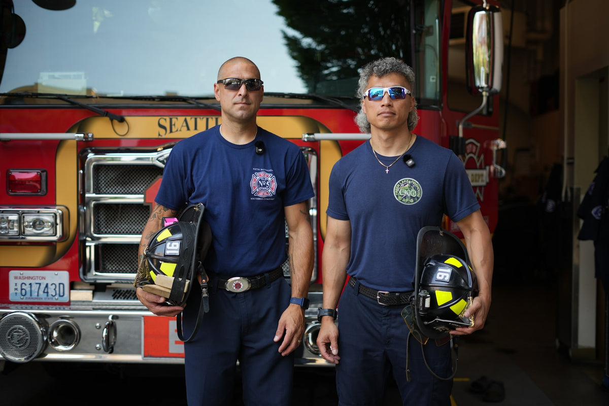 Two firefighters wearing Torque sunglasses and holding helmets beside their fire engine