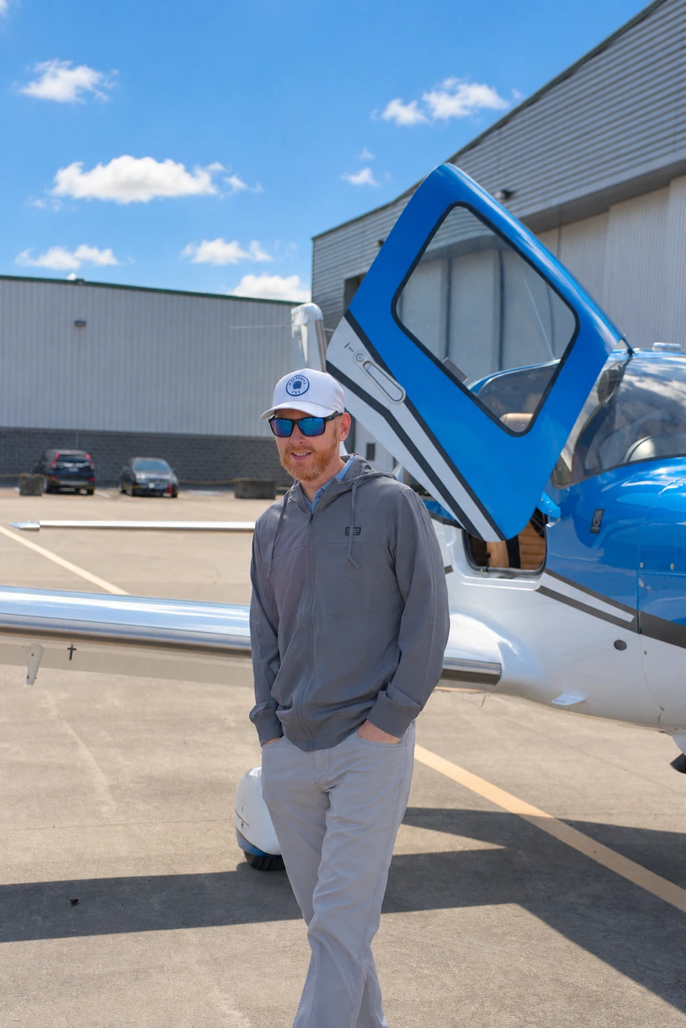 A man wearing Torque sunglasses beside a blue-and-white light aircraft with its door open.