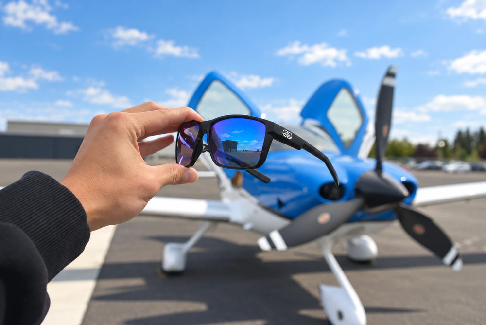 Torque sunglasses held in front of a blue-and-white light aircraft.