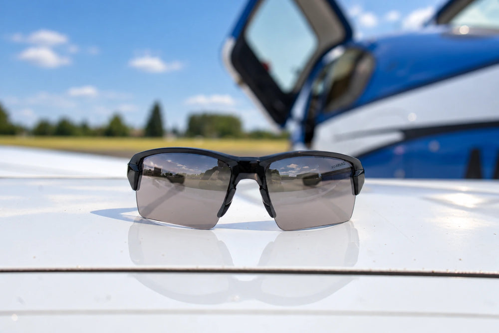 Black Torque Camber sunglasses with silver lenses resting on a white aircraft wing.