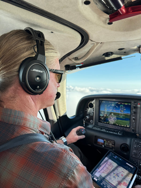 Bryan wearing sunglasses and a headset at the aircraft controls, with instruments and a tablet visible.