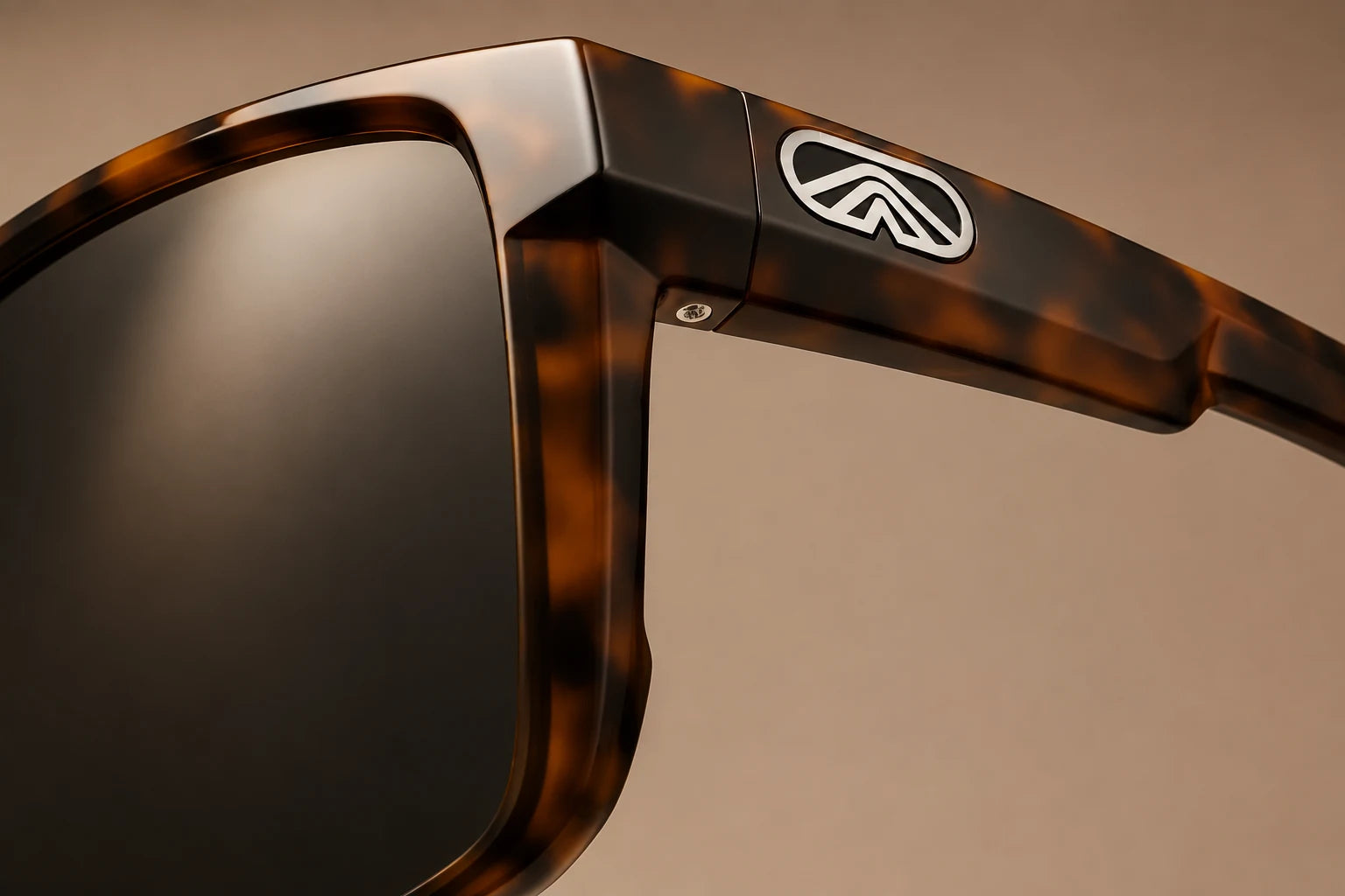Closeup of the polished smoke lens, amber tortoise Fulcrum frame and Torque emblem on warm taupe