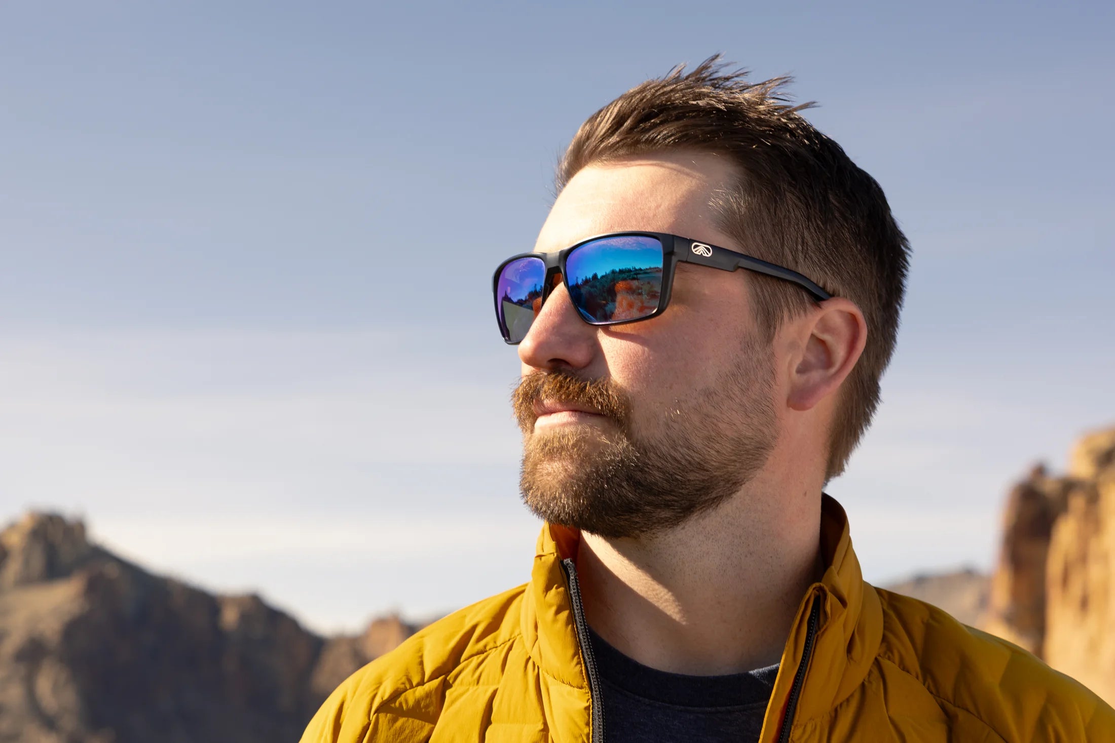 Man wearing blue mirrored Torque sunglasses and a yellow jacket in the mountains