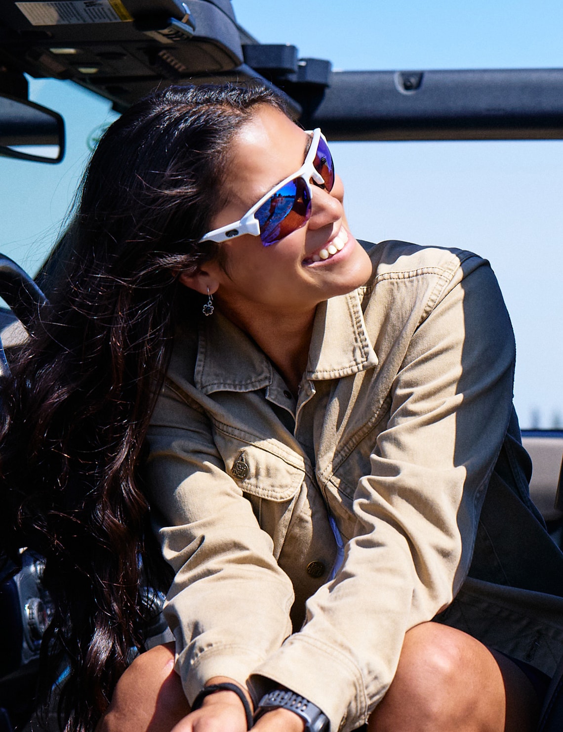 Smiling woman wearing white Torque sunglasses with blue mirrored lenses in a convertible