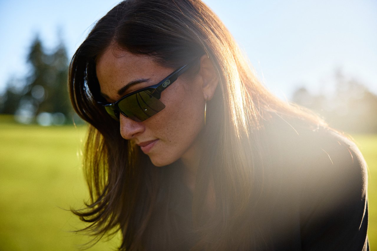 Woman wearing black Camber sunglasses on a sunlit golf course