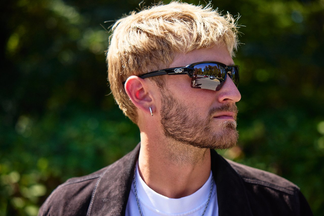 Blond man wearing black Camber sunglasses and a dark jacket outdoors