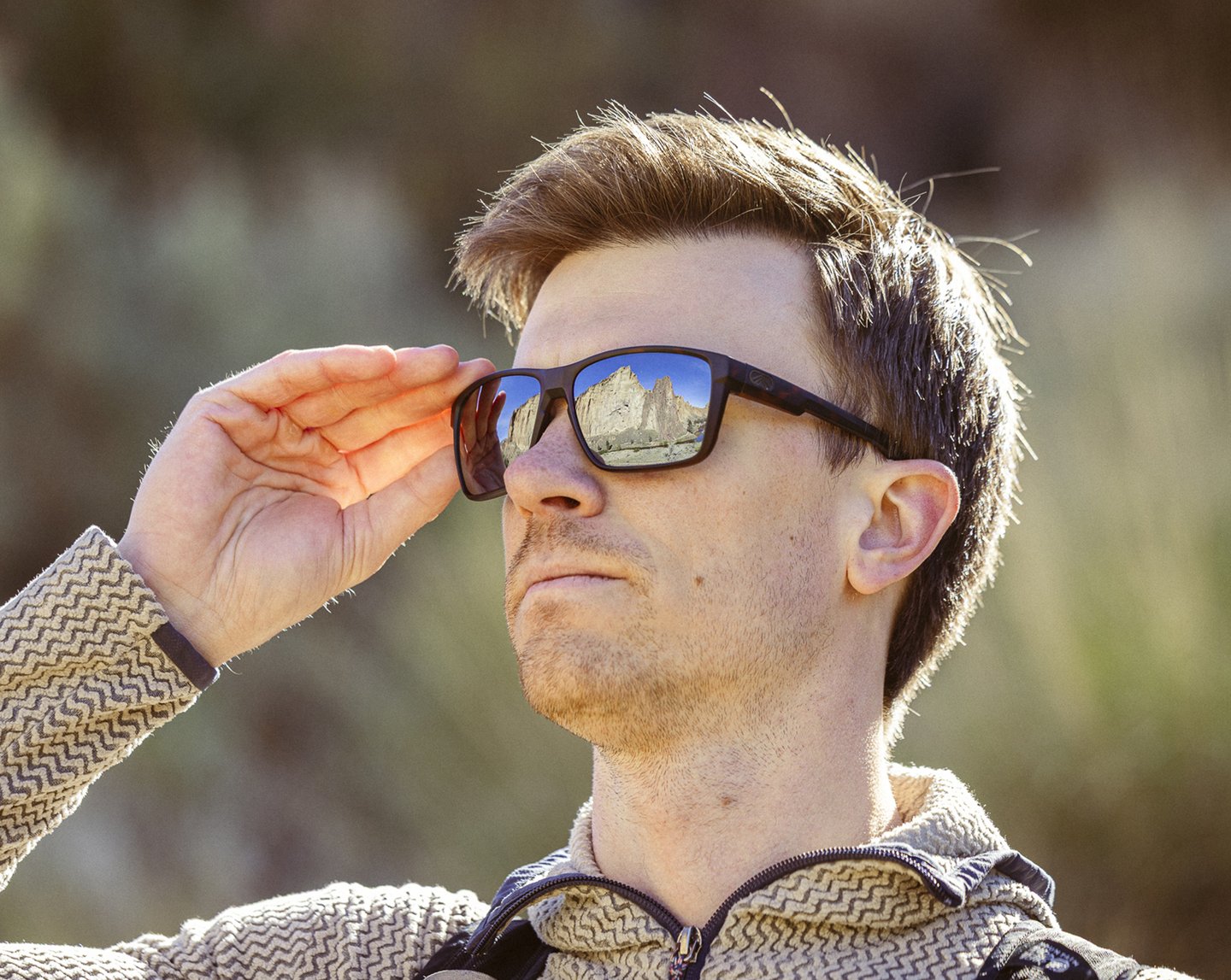 Person wearing Torque sunglasses outdoors, adjusting the frame while looking at a scenic vista.