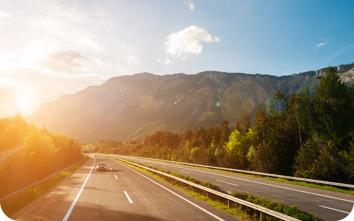 Sunlight over a mountain road surrounded by green forest.