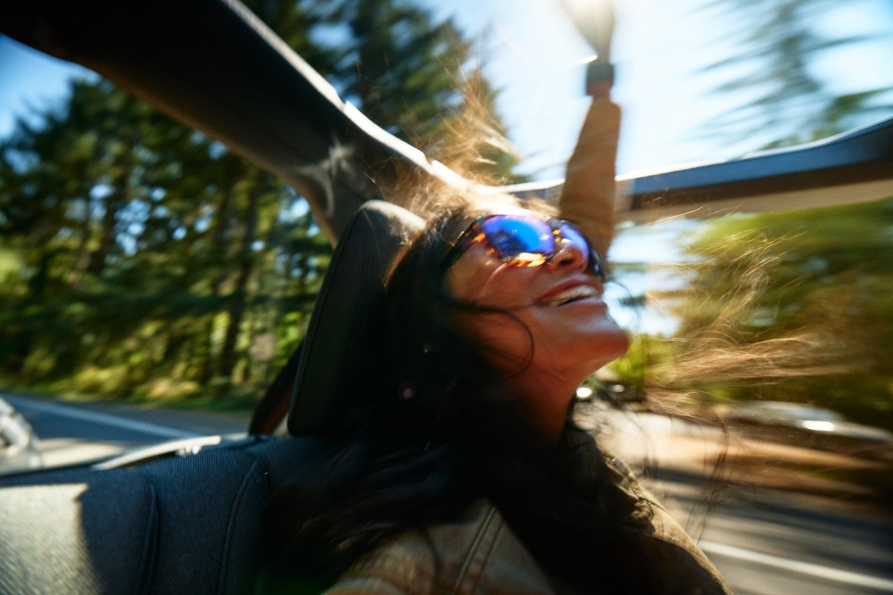 Woman wearing tortoise Fulcrum sunglasses with blue mirrored lenses in a sunlit convertible