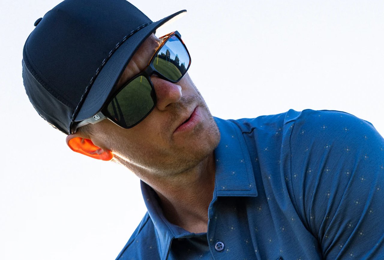 Man in a black cap and blue polo wearing Fulcrum sunglasses on a golf course
