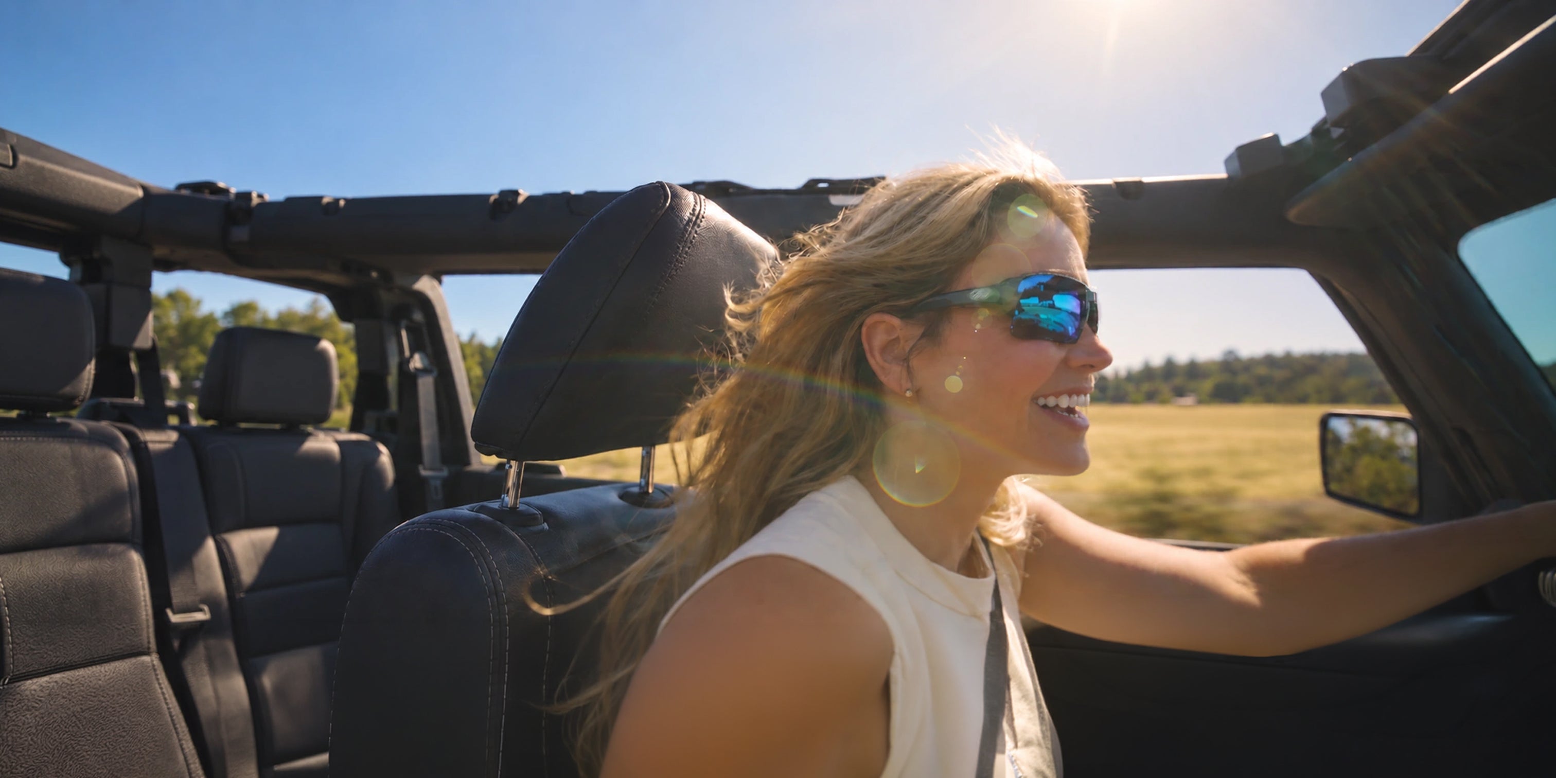 Smiling woman wearing blue mirrored Torque sunglasses while driving an open-top vehicle